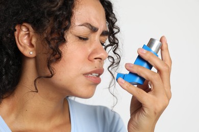 Photo of Young woman using asthma inhaler on white background, closeup