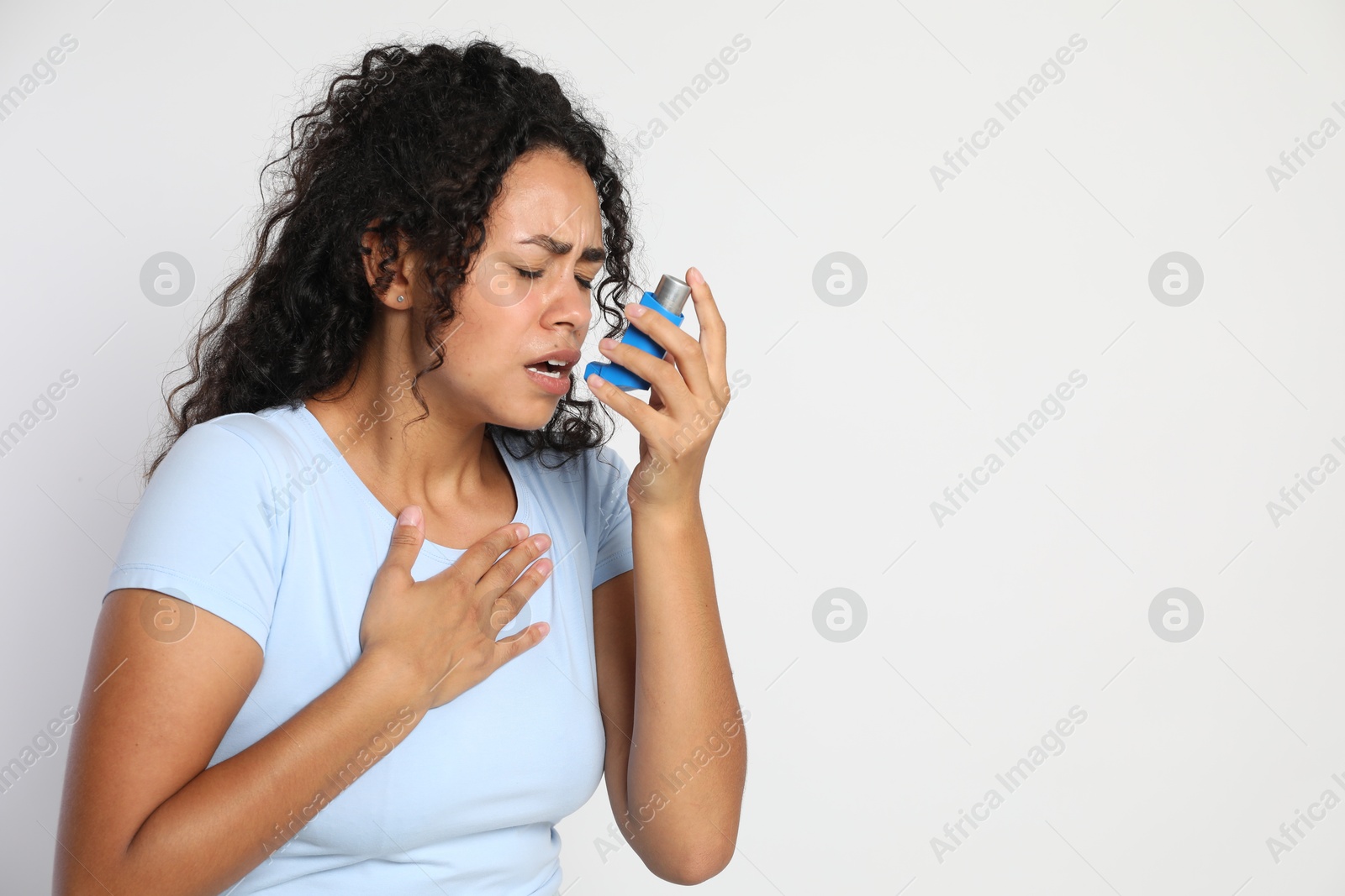 Photo of Young woman using asthma inhaler on white background. Space for text