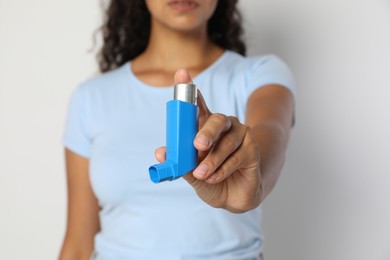 Photo of Woman holding asthma inhaler on light grey background, closeup