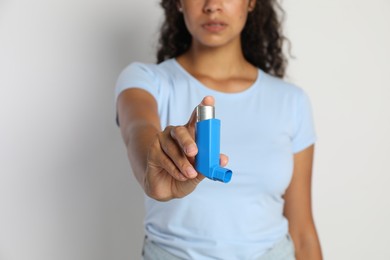 Photo of Woman holding asthma inhaler on light grey background, closeup