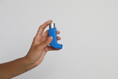 Woman holding asthma inhaler on light grey background, closeup. Space for text