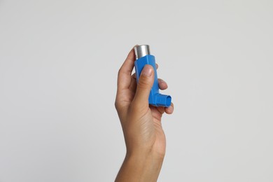 Photo of Woman holding asthma inhaler on light grey background, closeup