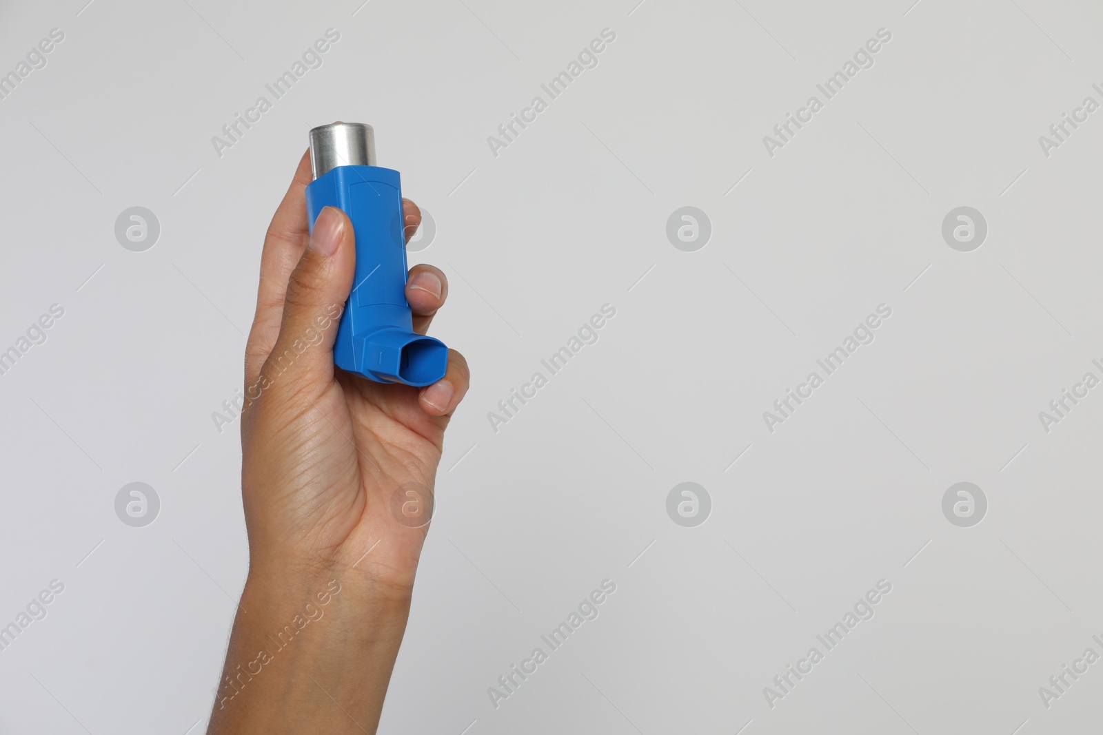 Photo of Woman holding asthma inhaler on light grey background, closeup. Space for text