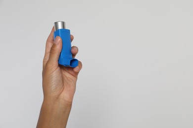 Woman holding asthma inhaler on light grey background, closeup. Space for text