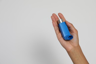 Photo of Woman holding asthma inhaler on light grey background, closeup. Space for text