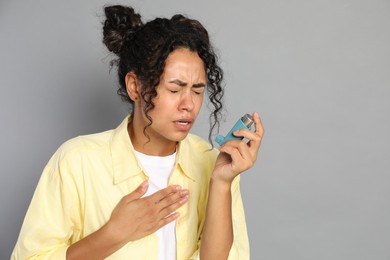 Photo of Young woman using asthma inhaler on grey background