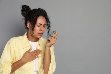 Young woman using asthma inhaler on grey background. Space for text