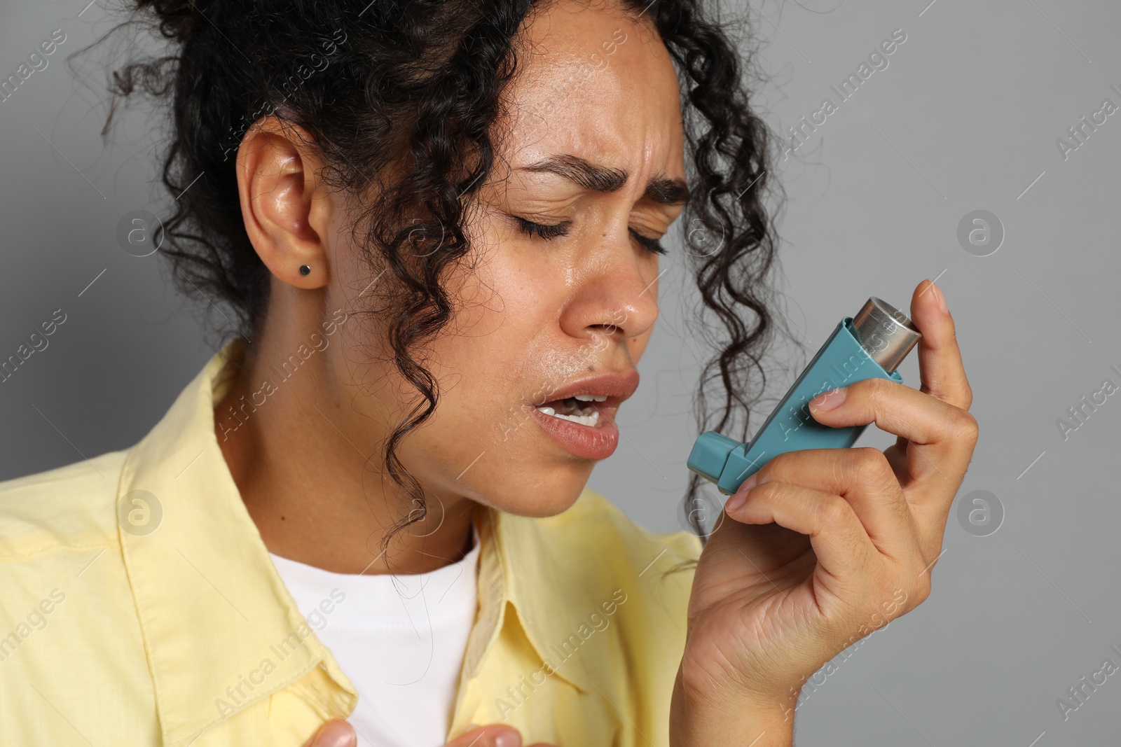 Photo of Young woman using asthma inhaler on grey background, closeup