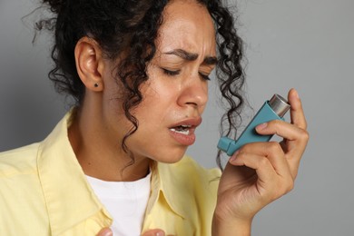 Young woman using asthma inhaler on grey background, closeup