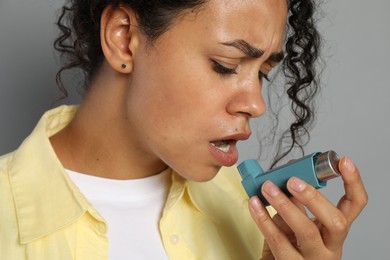 Young woman using asthma inhaler on grey background, closeup