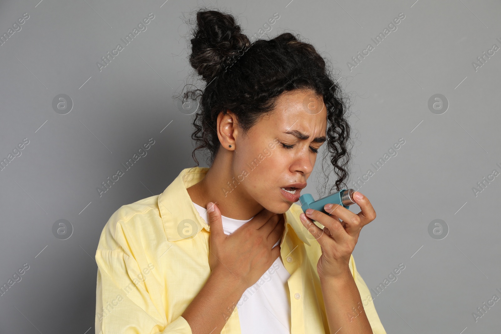 Photo of Young woman using asthma inhaler on grey background