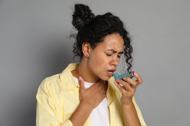 Young woman using asthma inhaler on grey background