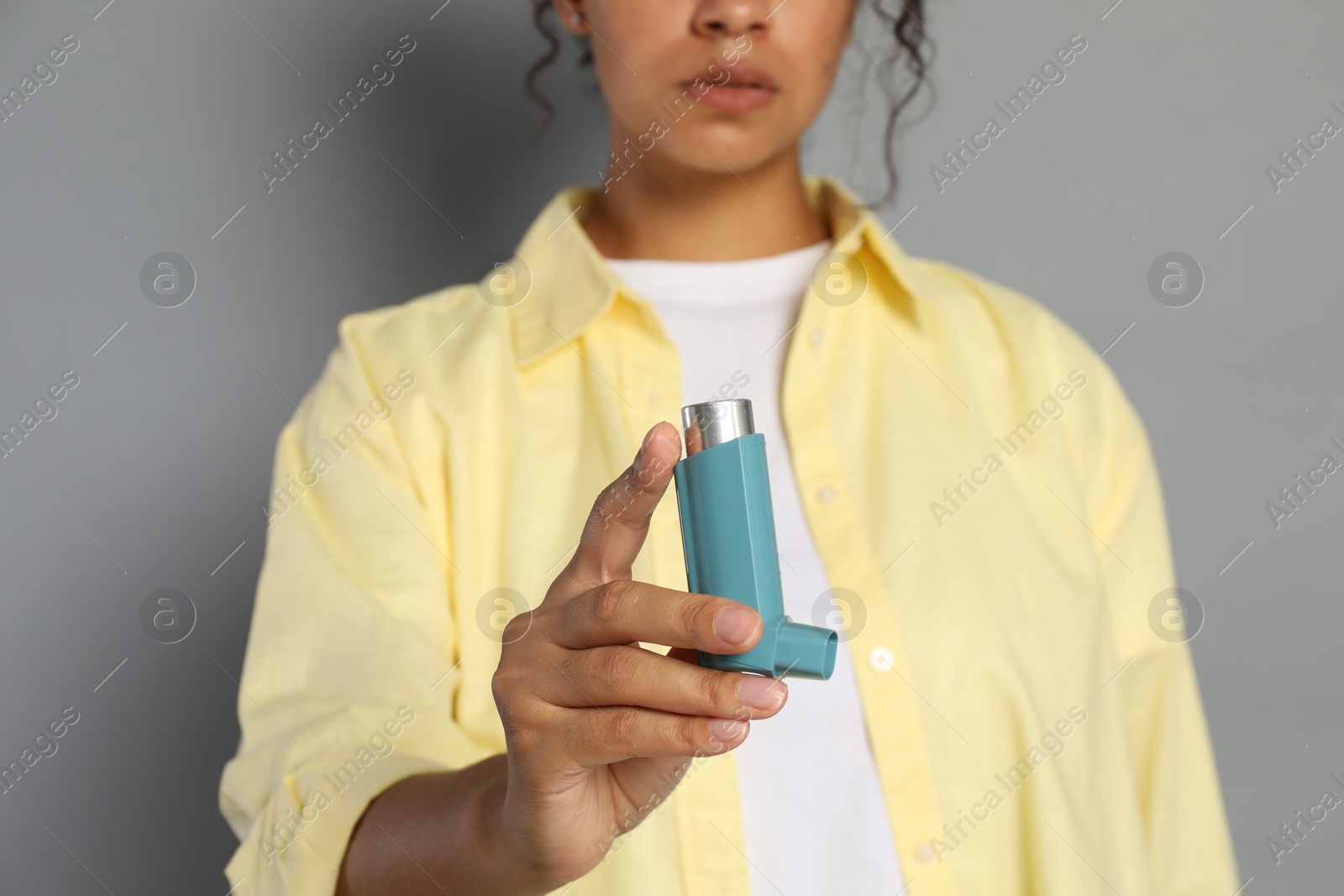 Photo of Woman holding asthma inhaler on grey background, closeup