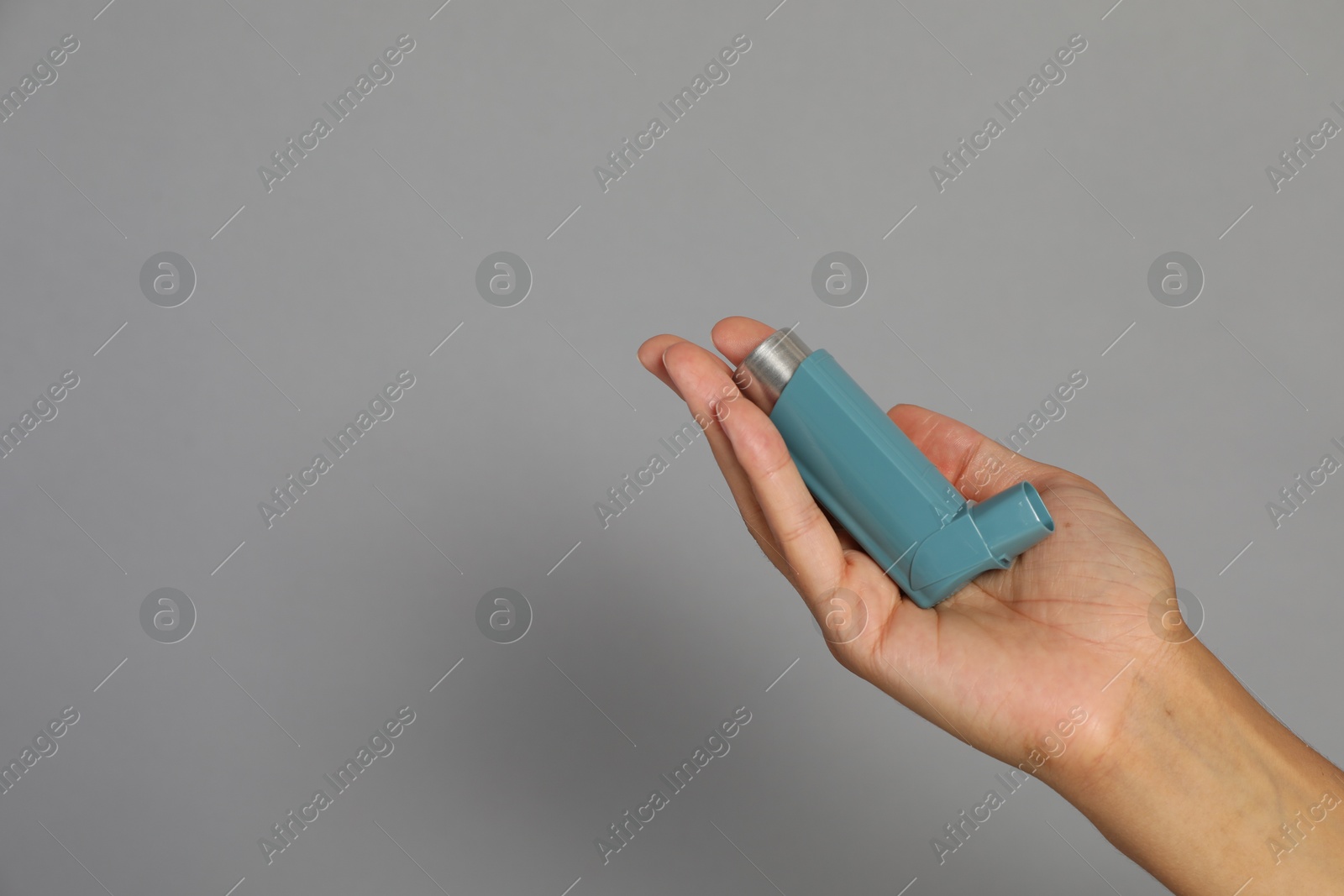 Photo of Woman holding asthma inhaler on grey background, closeup. Space for text