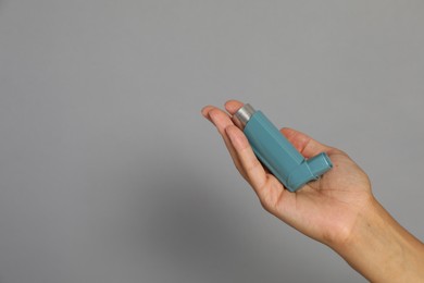 Photo of Woman holding asthma inhaler on grey background, closeup. Space for text