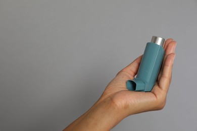 Photo of Woman holding asthma inhaler on grey background, closeup. Space for text