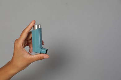 Photo of Woman holding asthma inhaler on grey background, closeup. Space for text