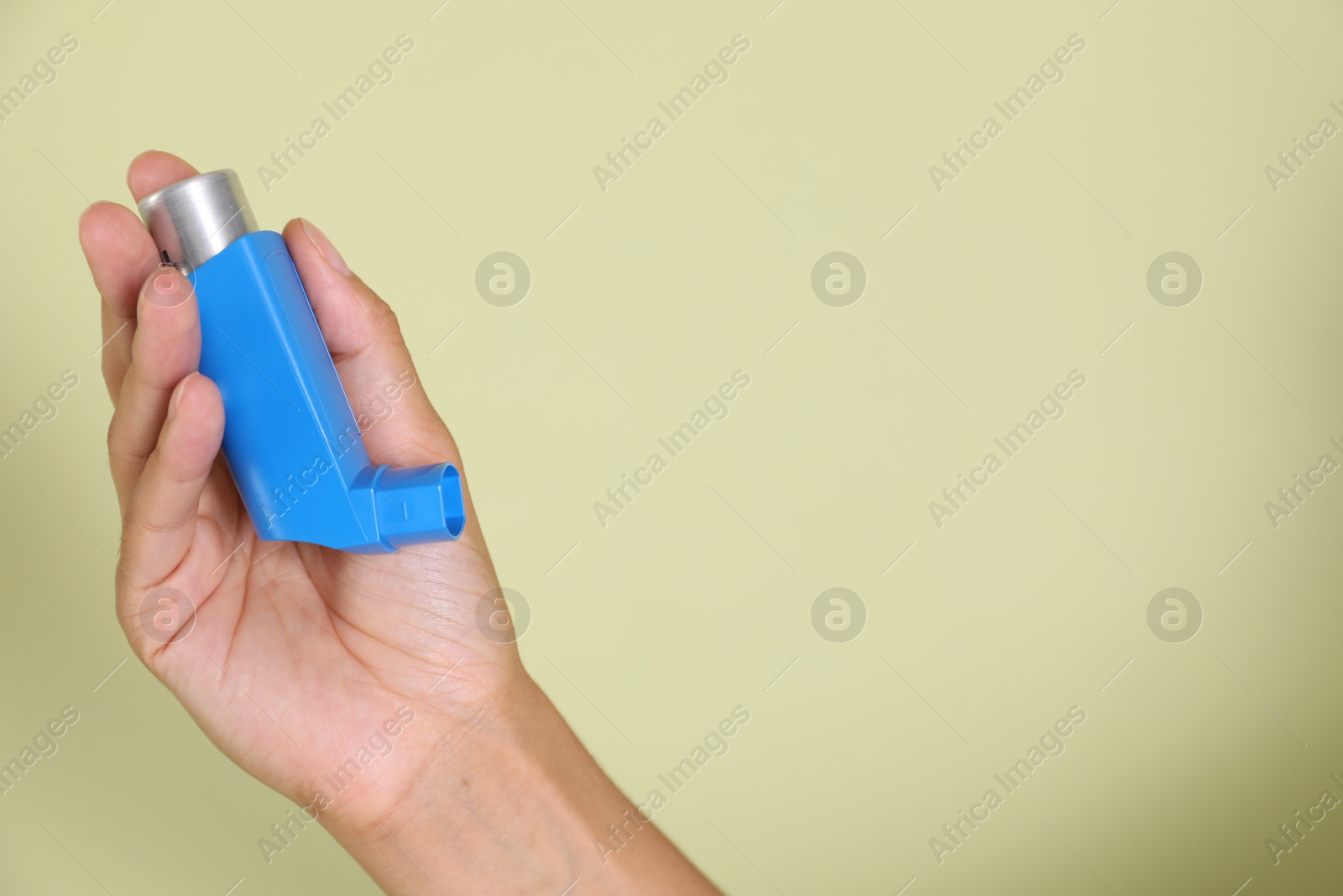 Photo of Woman holding asthma inhaler on light olive background, closeup. Space for text