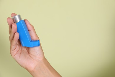 Woman holding asthma inhaler on light olive background, closeup. Space for text