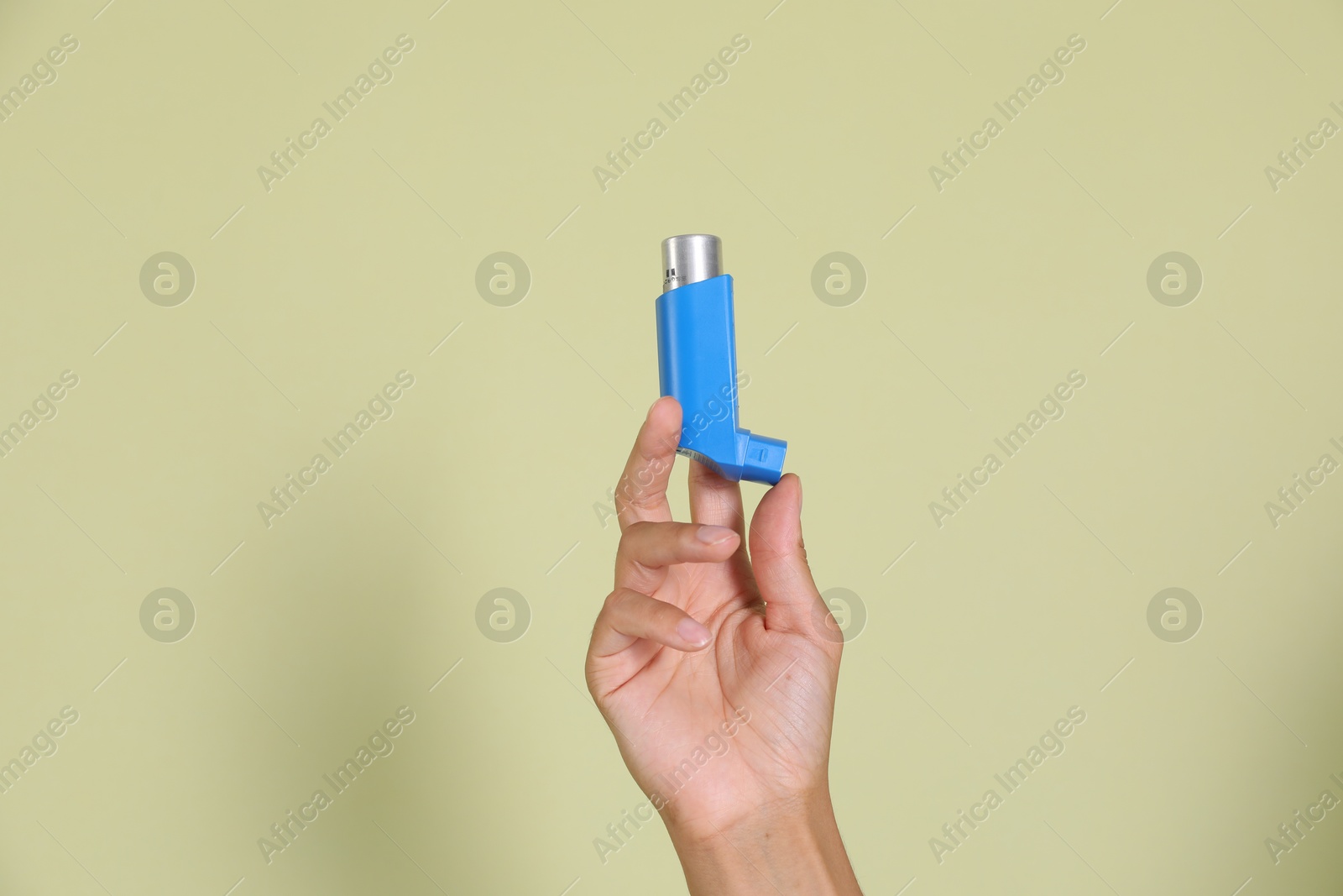 Photo of Woman holding asthma inhaler on light olive background, closeup