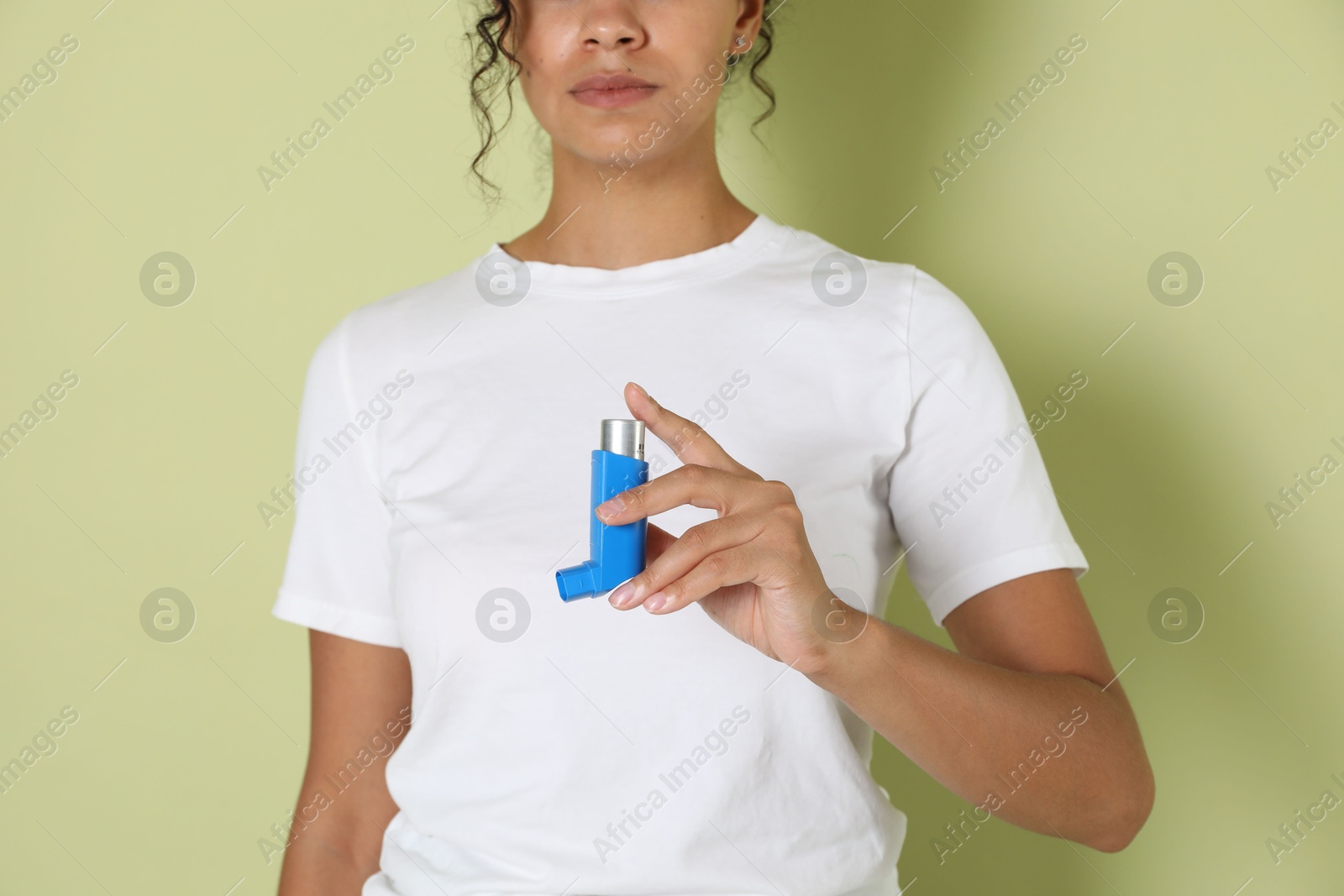 Photo of Woman holding asthma inhaler on light olive background, closeup