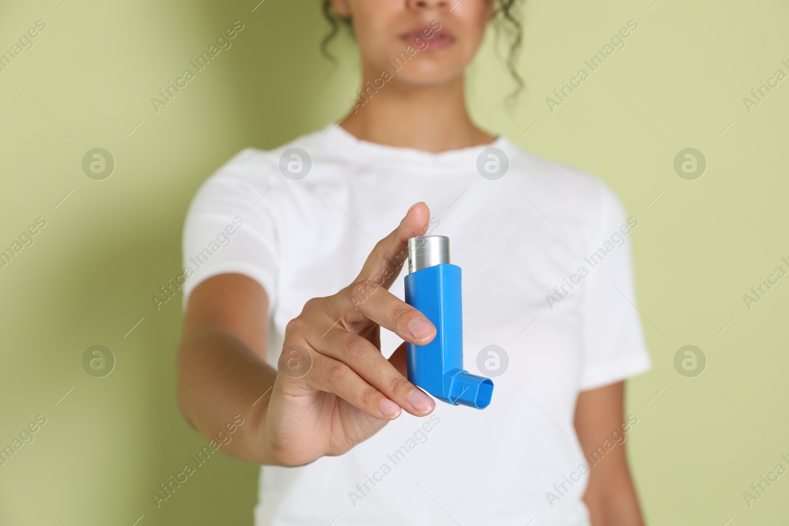 Photo of Woman holding asthma inhaler on light olive background, closeup