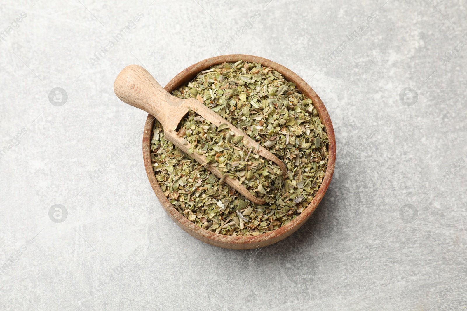 Photo of Dried oregano and scoop in wooden bowl on grey table, top view