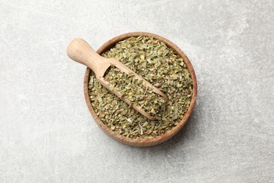 Photo of Dried oregano and scoop in wooden bowl on grey table, top view