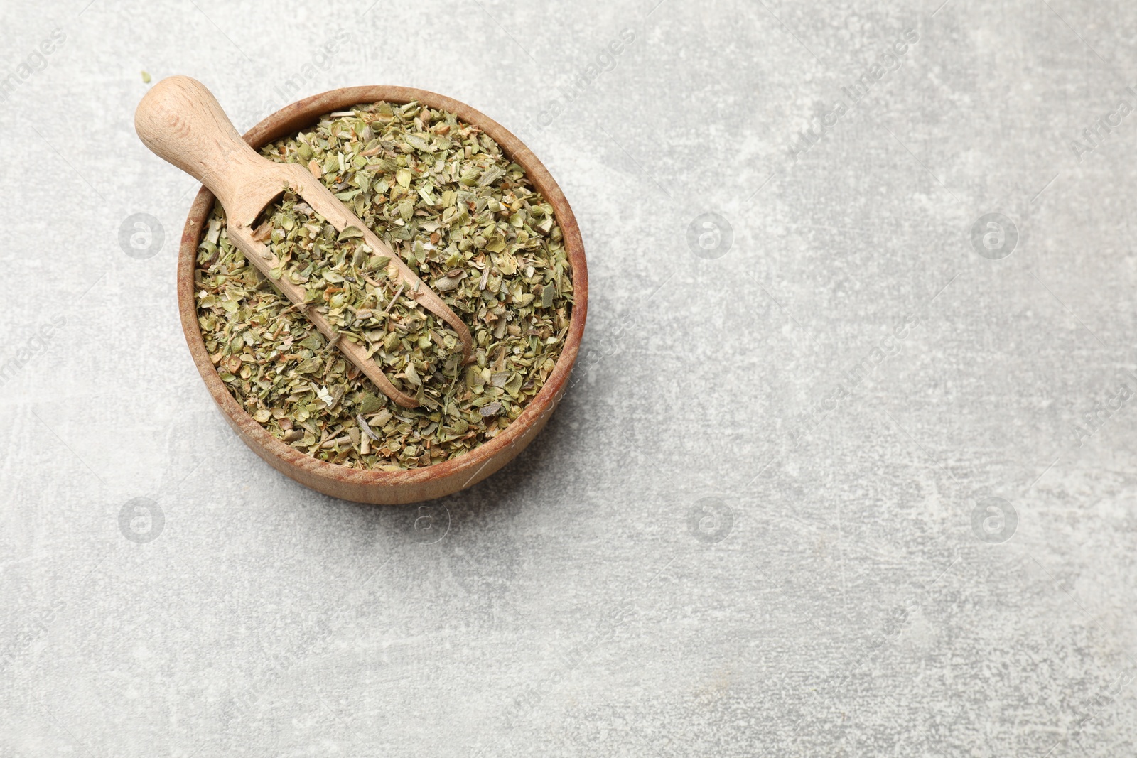 Photo of Dried oregano and scoop in wooden bowl on grey table, top view. Space for text