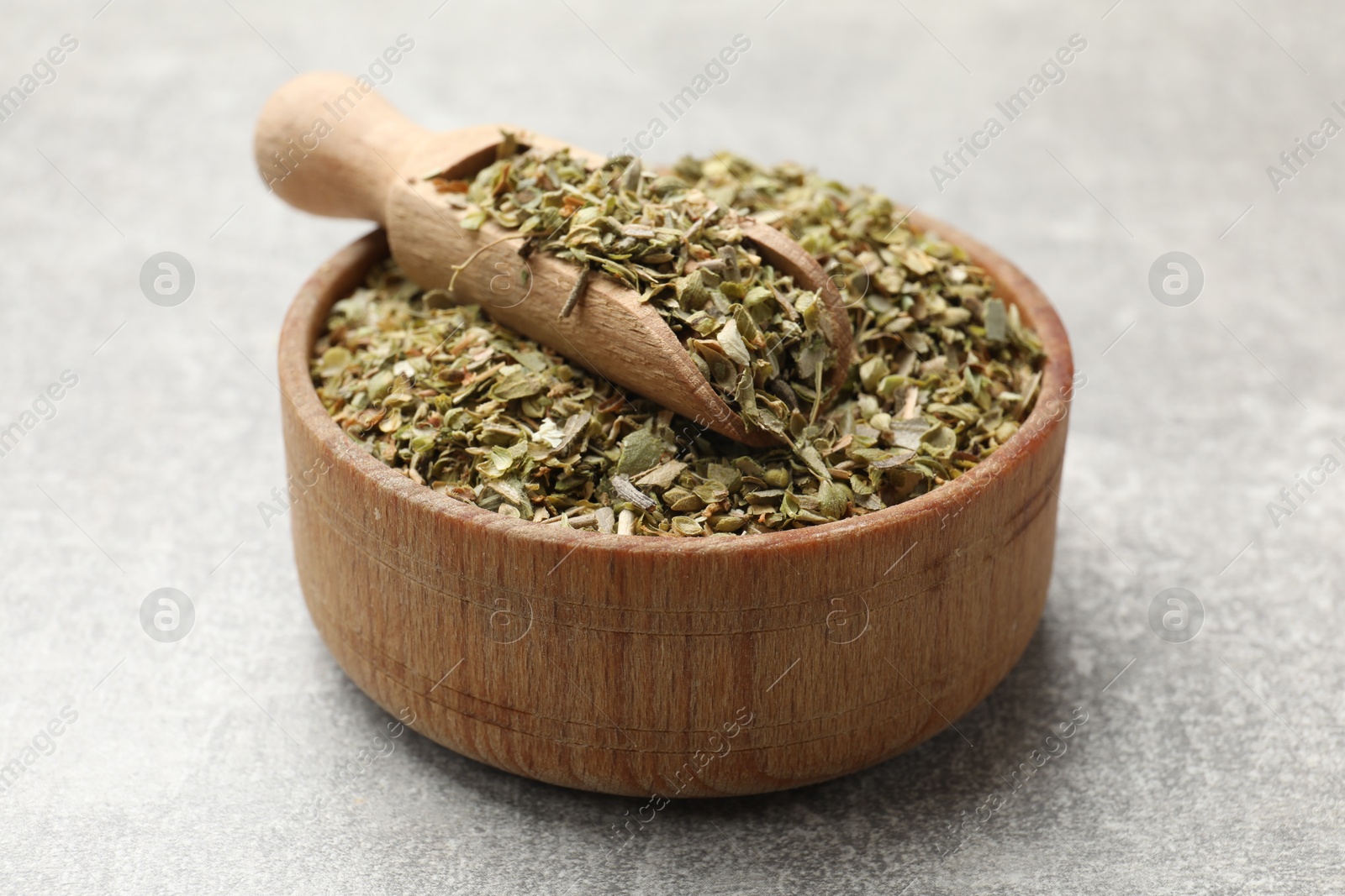 Photo of Dried oregano and scoop in wooden bowl on grey table, closeup