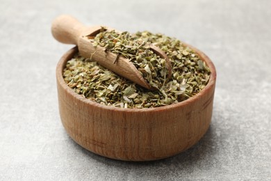 Dried oregano and scoop in wooden bowl on grey table, closeup