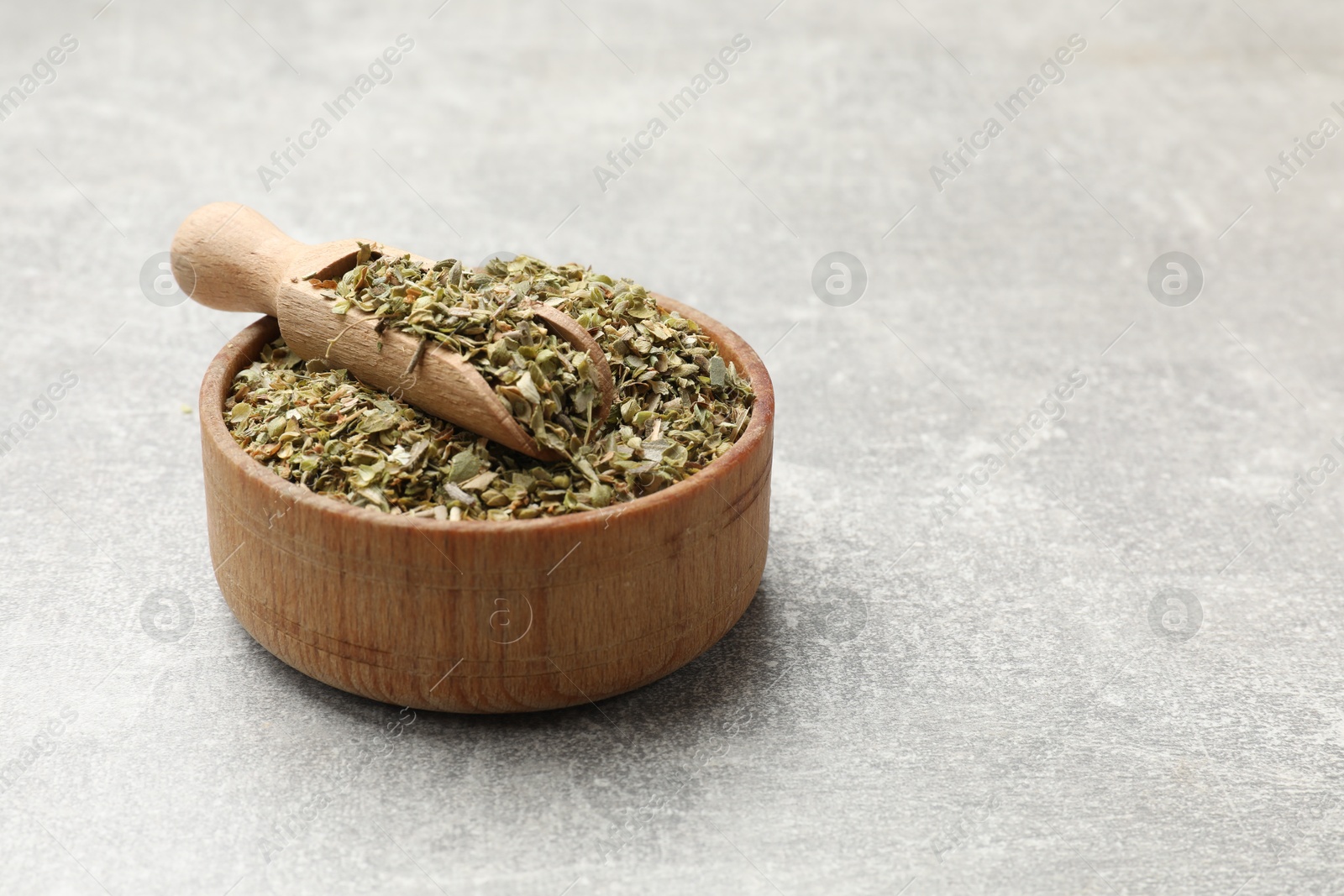 Photo of Dried oregano and scoop in wooden bowl on grey table, closeup. Space for text