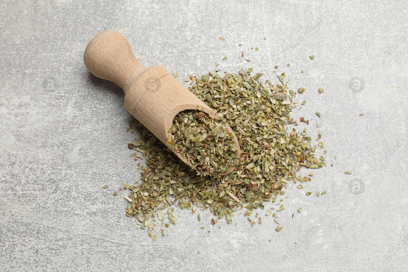 Photo of Wooden scoop with dried oregano on grey table, top view