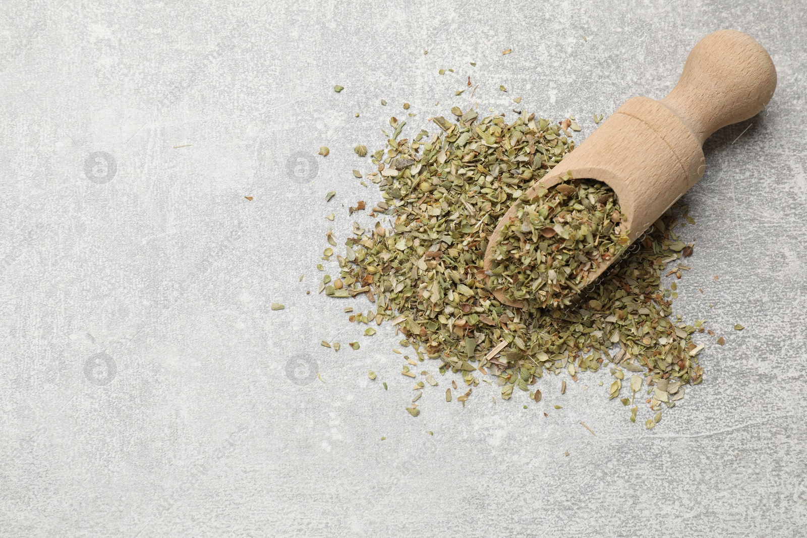 Photo of Wooden scoop with dried oregano on grey table, top view. Space for text