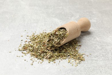 Wooden scoop with dried oregano on grey table, closeup