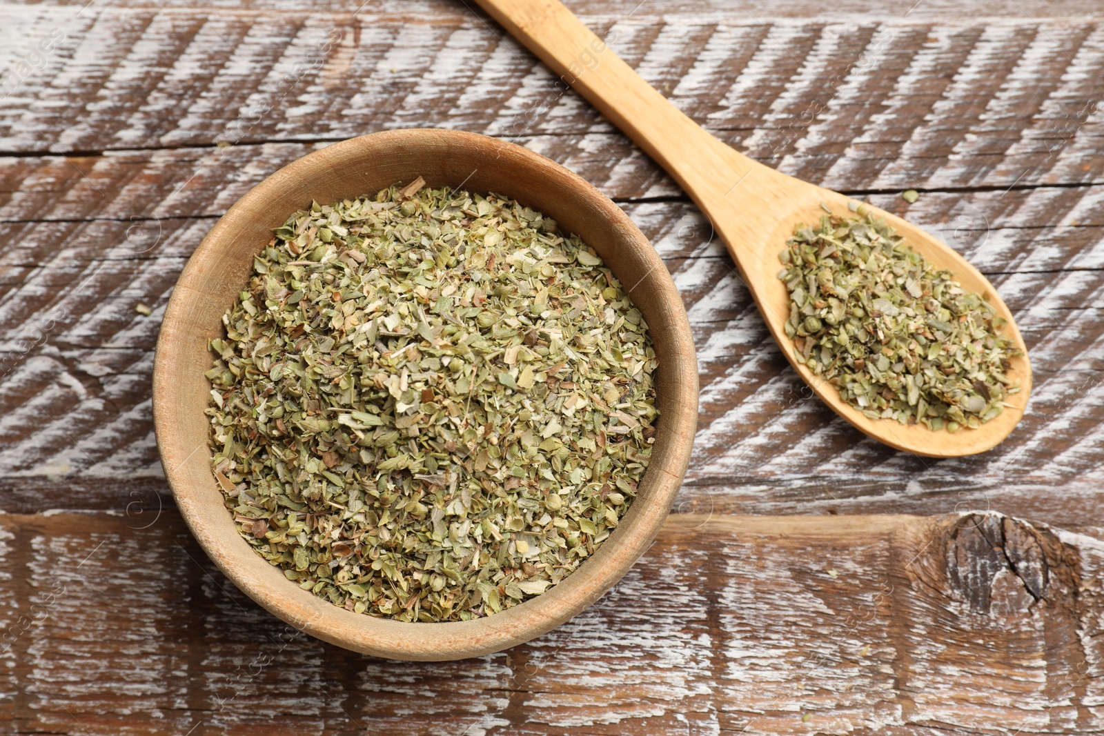 Photo of Dried oregano in bowl and spoon on wooden table, top view