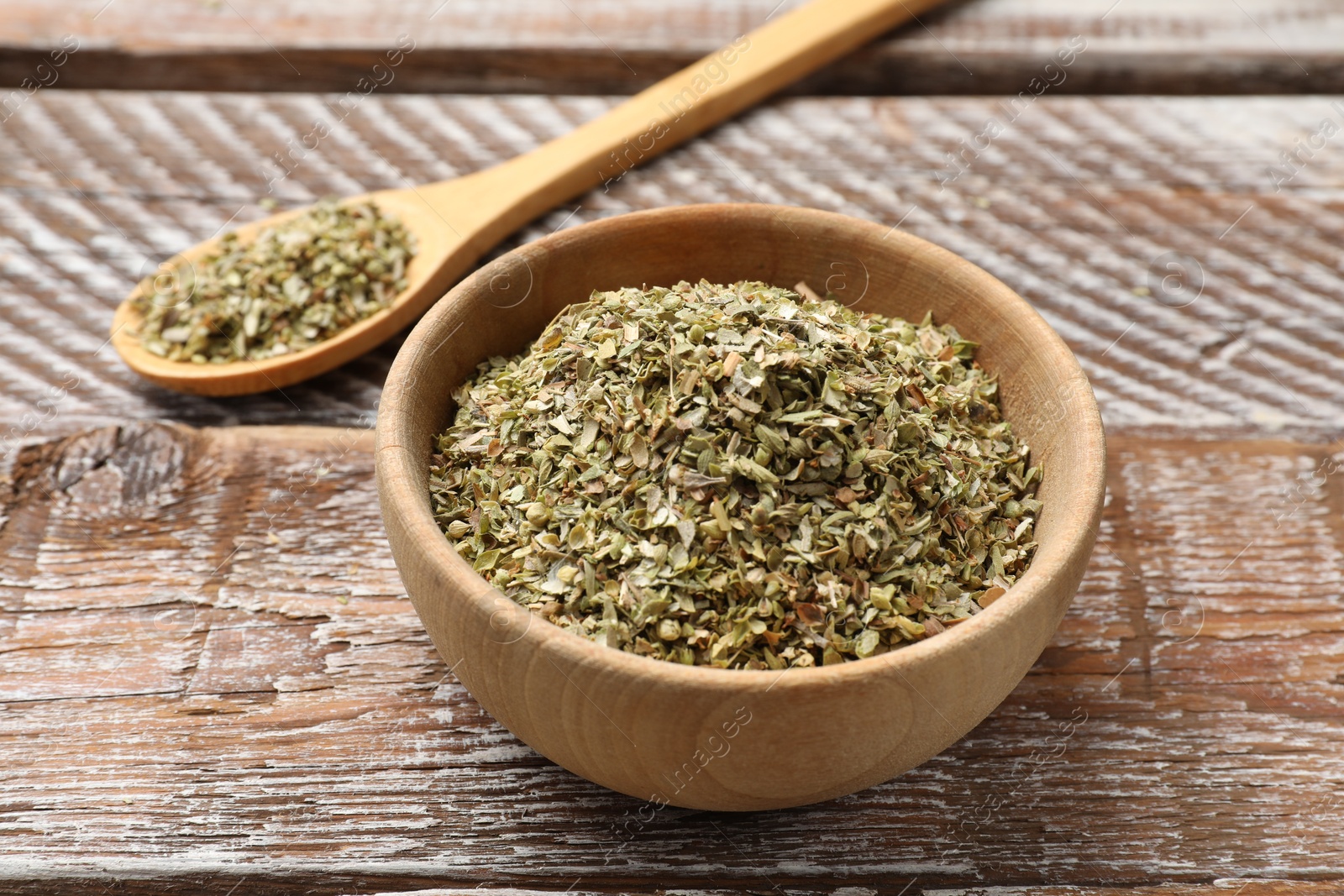 Photo of Dried oregano in bowl and spoon on wooden table, closeup