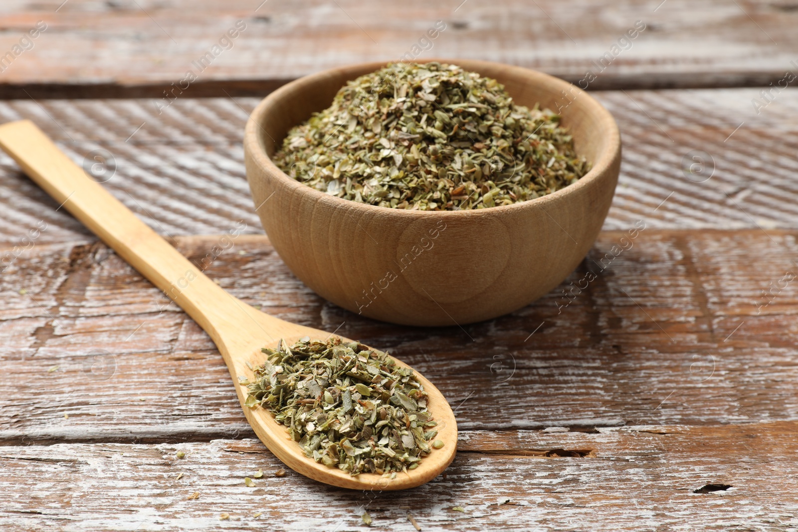 Photo of Dried oregano in bowl and spoon on wooden table, closeup