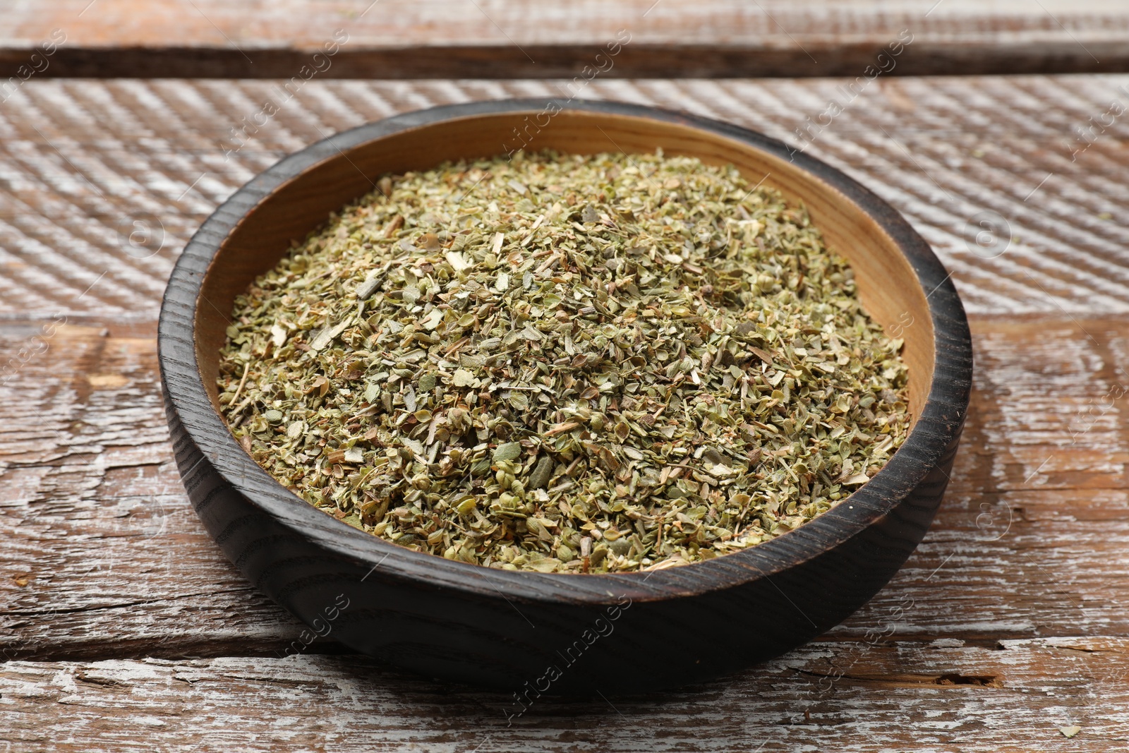 Photo of Dried oregano in bowl on wooden table, closeup