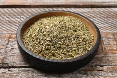 Dried oregano in bowl on wooden table, closeup