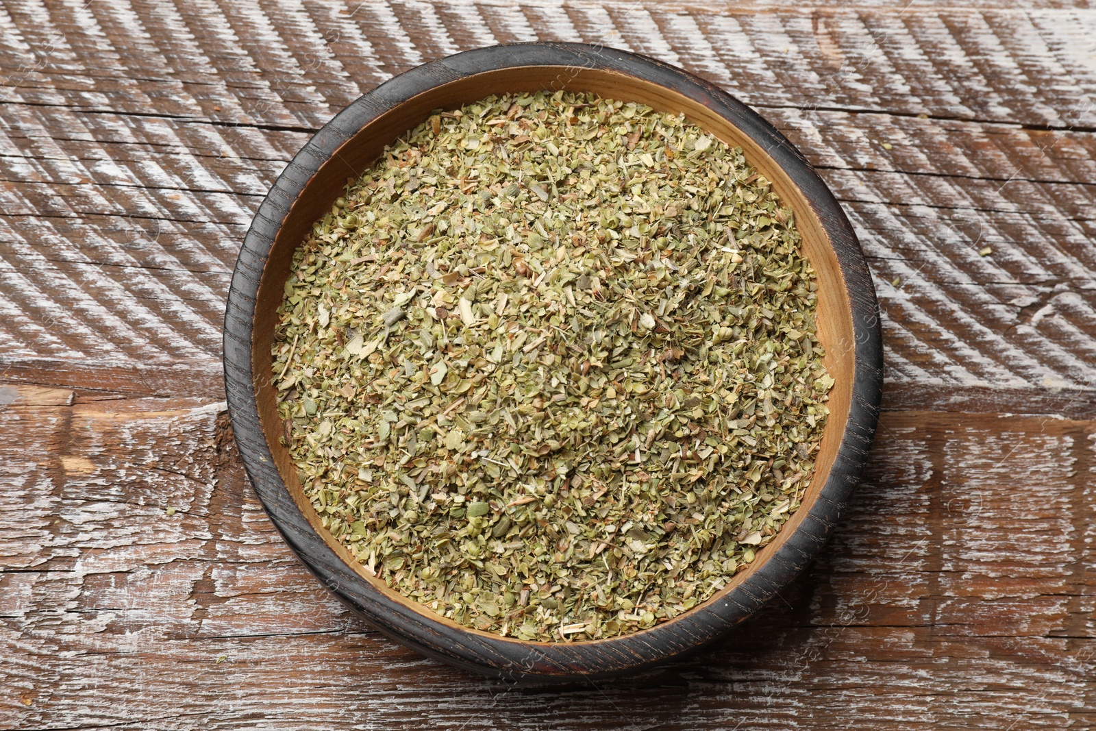 Photo of Dried oregano in bowl on wooden table, top view