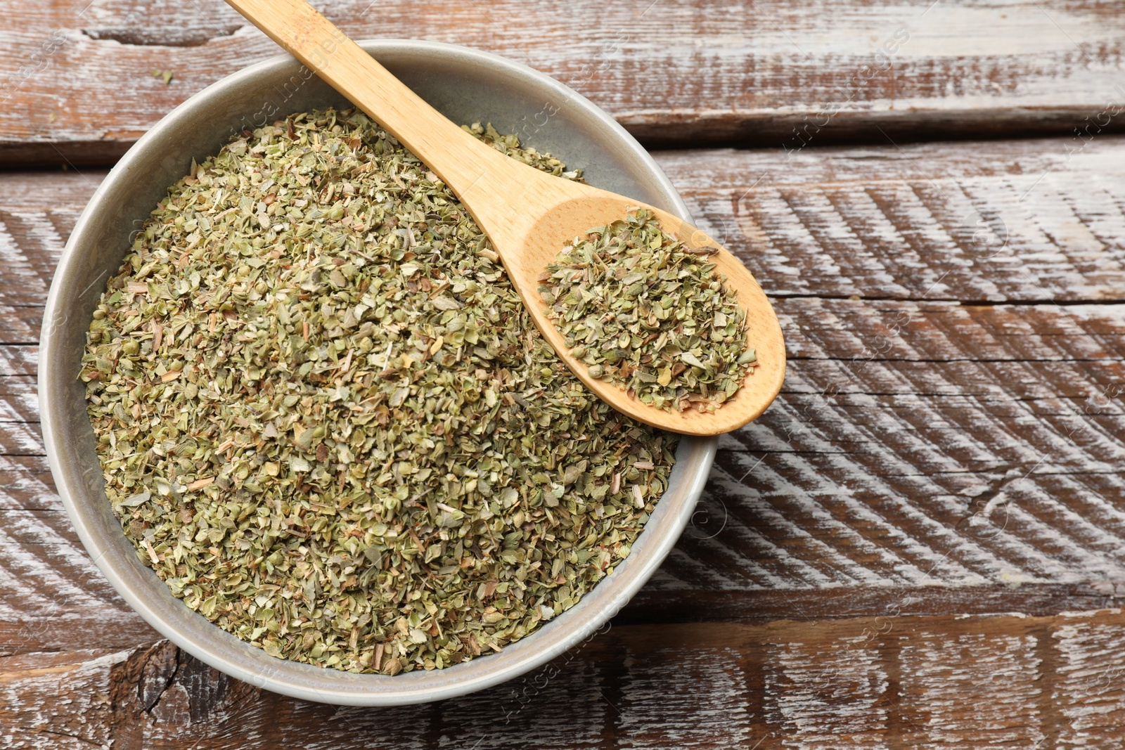 Photo of Dried oregano in bowl and spoon on wooden table, top view. Space for text