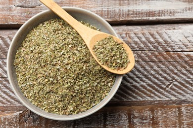 Dried oregano in bowl and spoon on wooden table, top view. Space for text