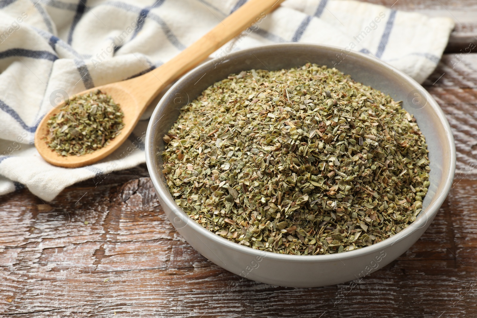 Photo of Dried oregano in bowl and spoon on wooden table, closeup