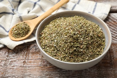 Photo of Dried oregano in bowl and spoon on wooden table, closeup