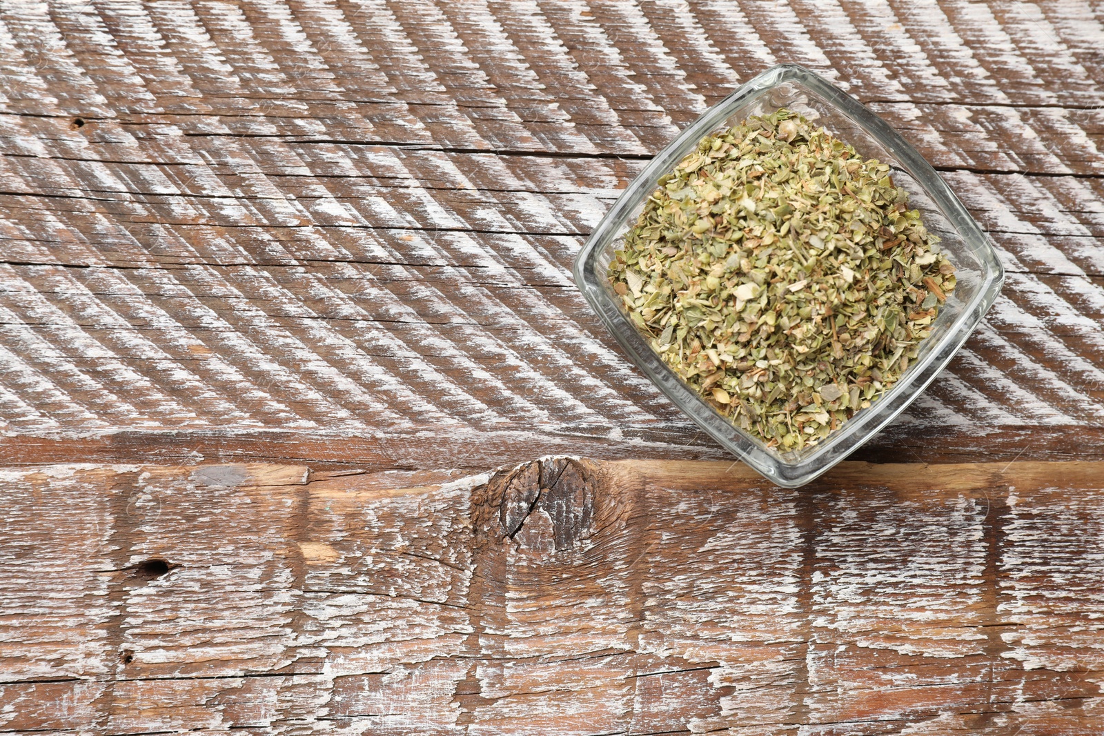 Photo of Dried oregano in bowl on wooden table, top view. Space for text