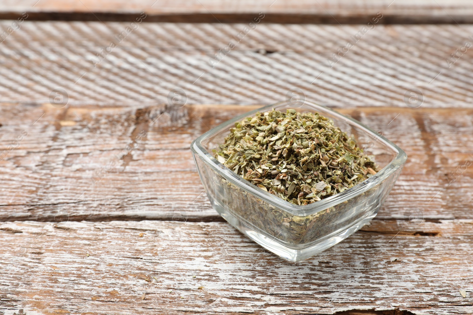 Photo of Dried oregano in bowl on wooden table, closeup. Space for text