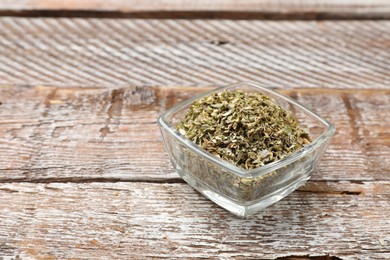 Dried oregano in bowl on wooden table, closeup. Space for text