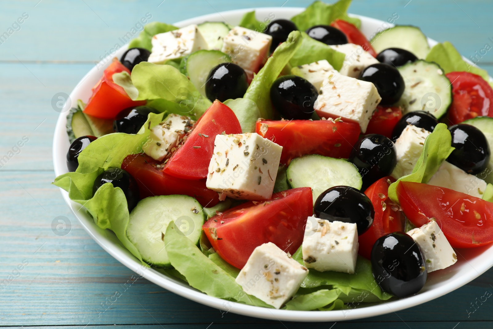 Photo of Delicious salad with feta cheese on light blue wooden table, closeup