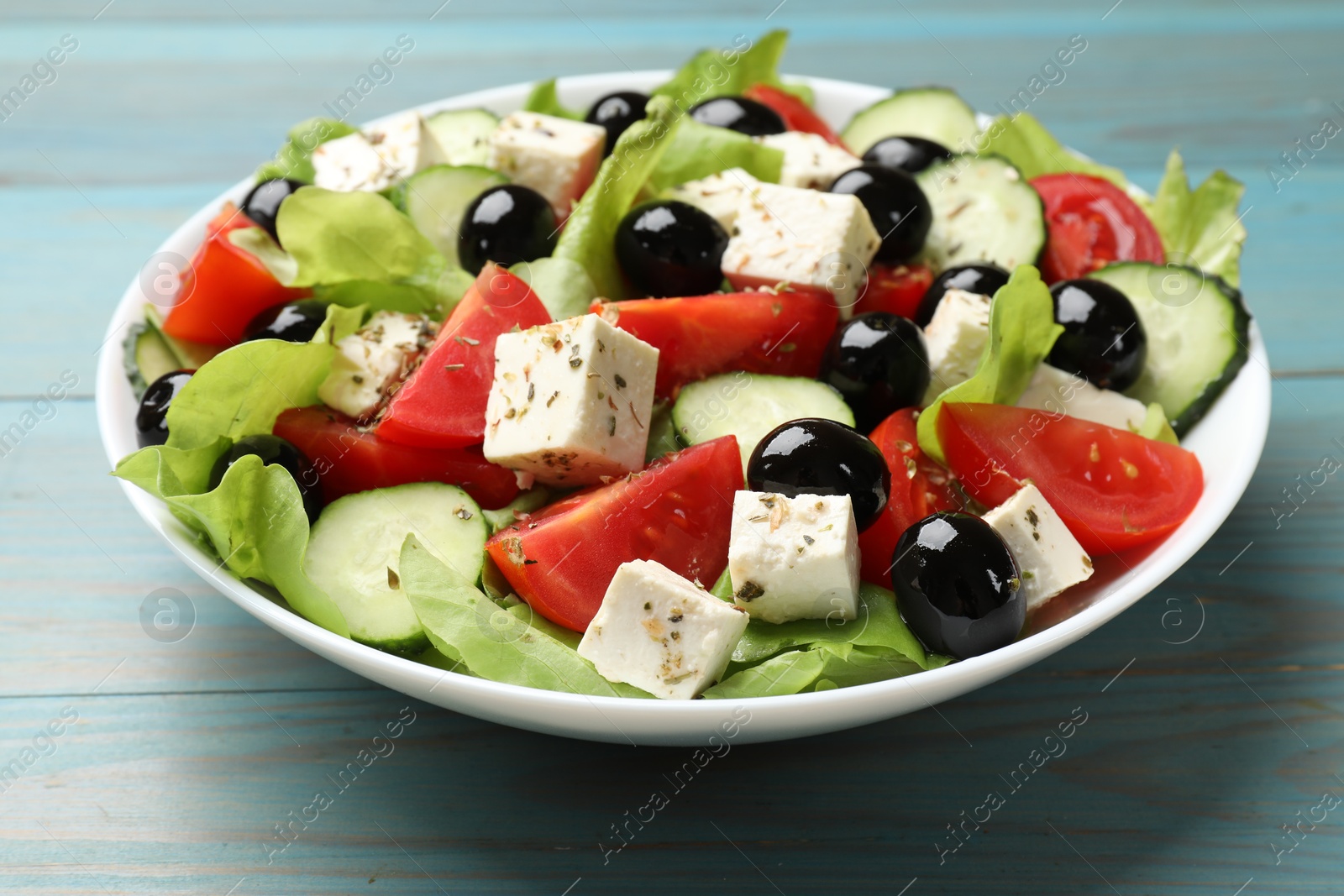 Photo of Delicious salad with feta cheese on light blue wooden table, closeup